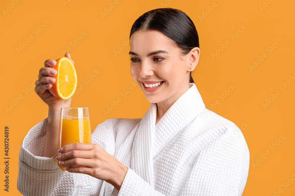 Beautiful young woman making fresh orange juice on color background