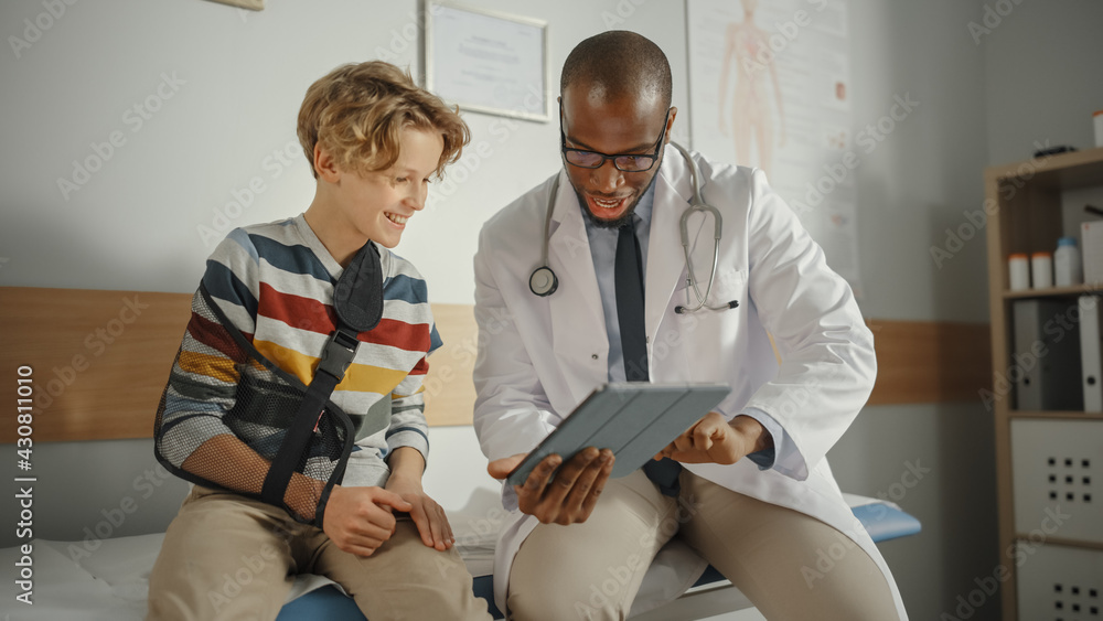 Friendly African American Family Doctor Talking with a Young Boy with Arm Brace and Showing Test Res