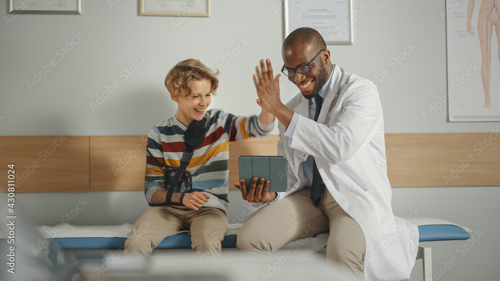 Friendly African American Family Doctor Talking with a Young Boy with Arm Brace, Showing Test Result