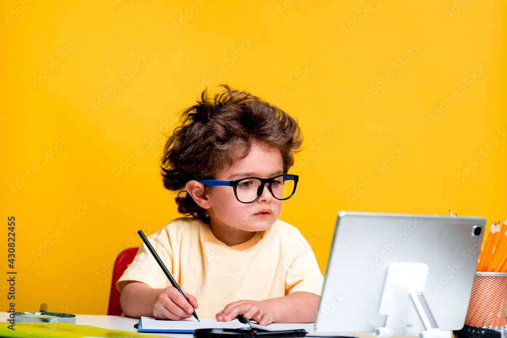 Portrait of smart school kid boy at home making homework with tablet computer. Little child in glass