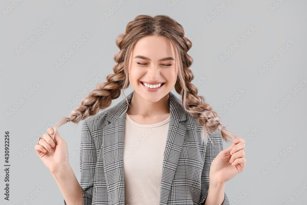 Beautiful young woman with braided hair on grey background