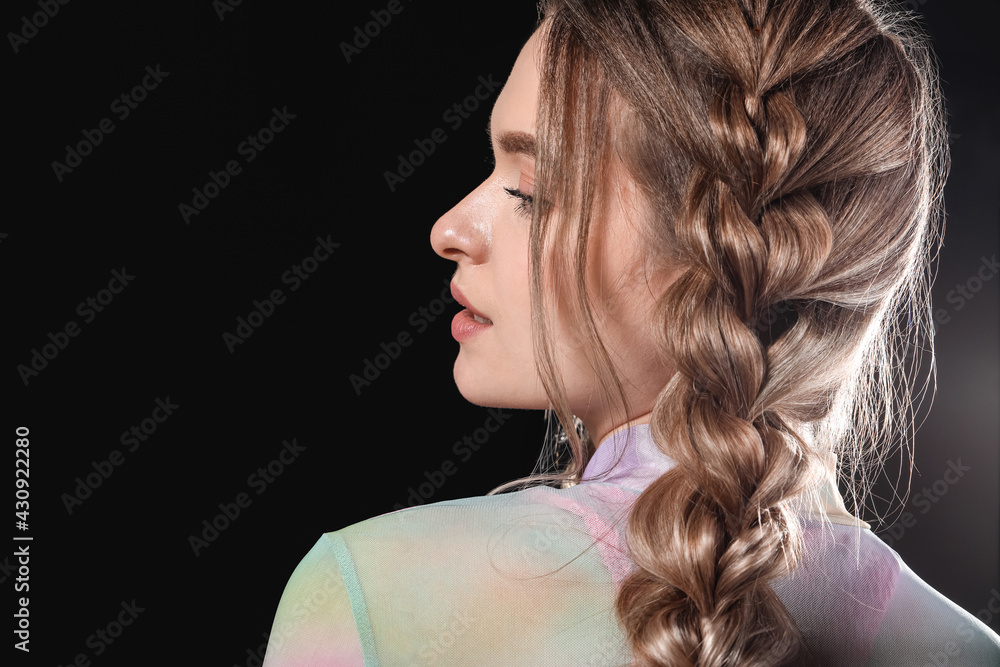 Beautiful young woman with braided hair on dark background