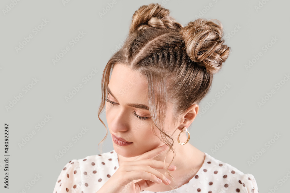 Beautiful young woman with braided hair on grey background