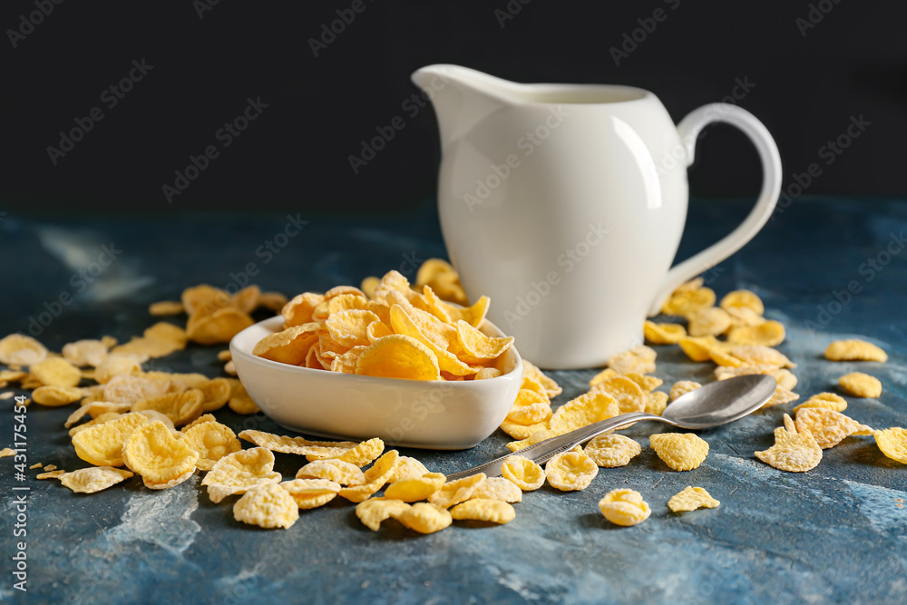 Bowl with tasty cornflakes and jug with milk on color background