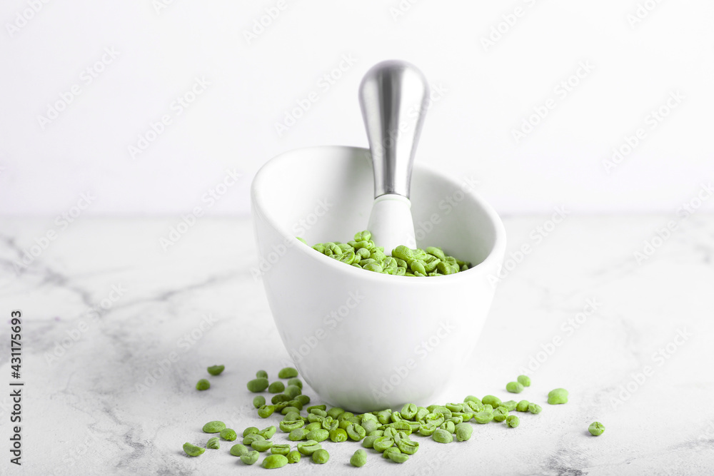 Mortar and pestle with green coffee beans on light background