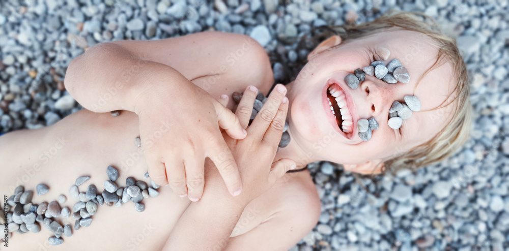 On sunny beach happy kids have fun, lying down on hot pebble, sunbathing, warming after swimming in 