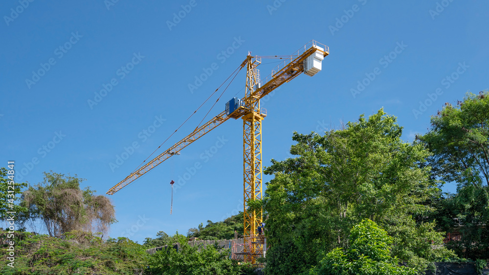 Working construction crane with green trees forest and blue sky background Industrial concept