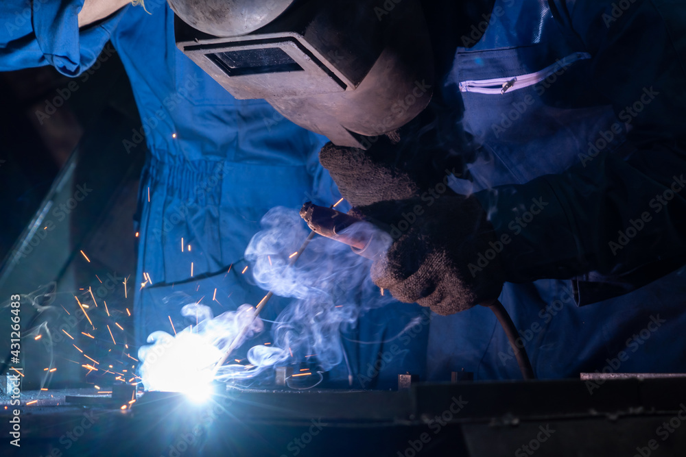 Skillful metal worker working with arc welding machine in factory while wearing safety equipment. Me