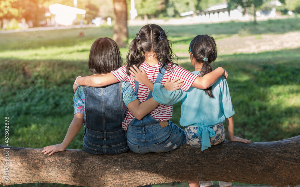 Children friendship concept with happy girl kids in the park having fun sitting under tree shade pla