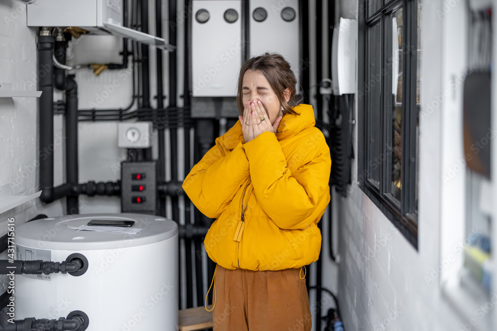 Young woman feeling cold, wearing jacket in the boiler room. Housewife adjusts temperature on the ga