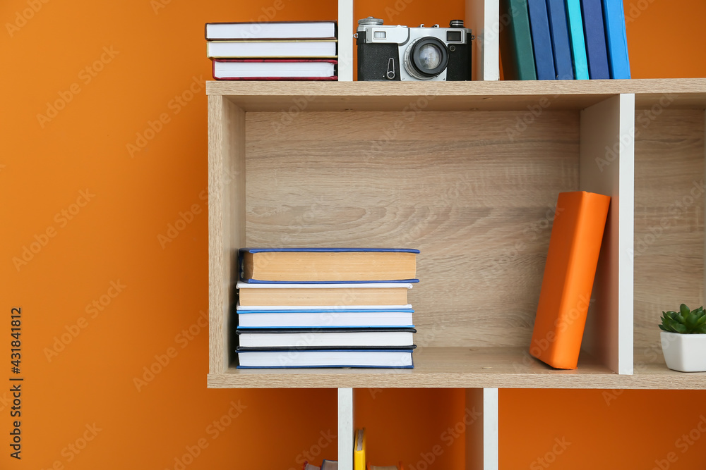 Shelf unit with books and decor on color background