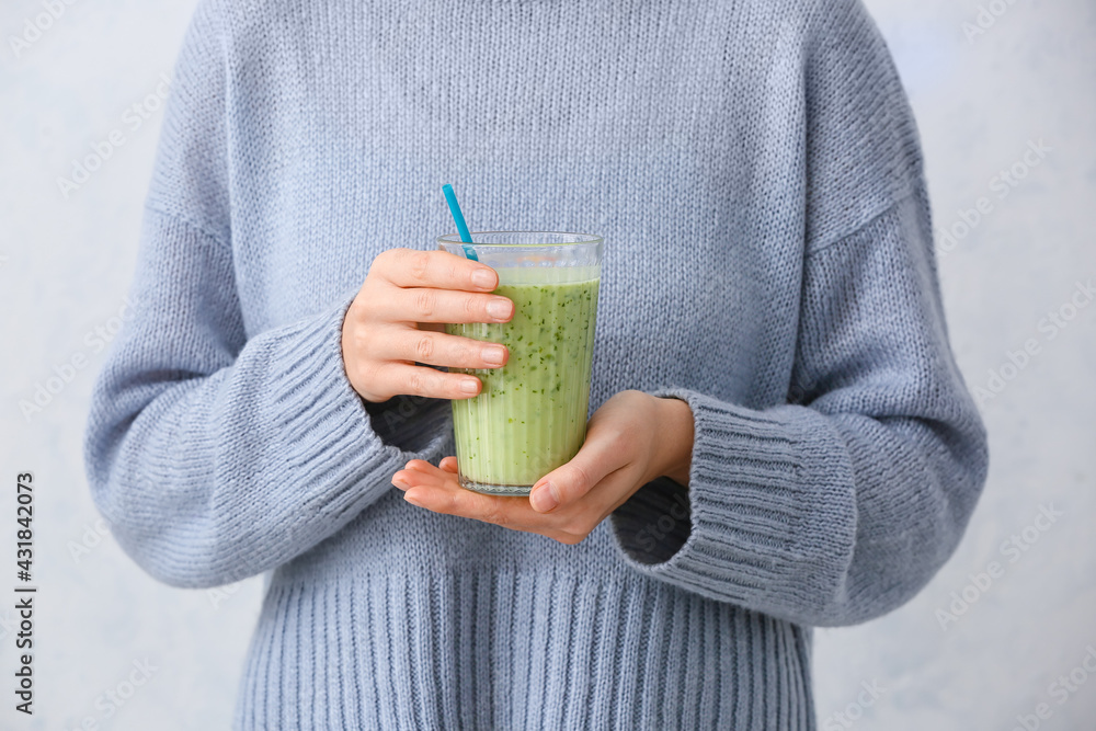 Woman with glass of fruit smoothie on light background