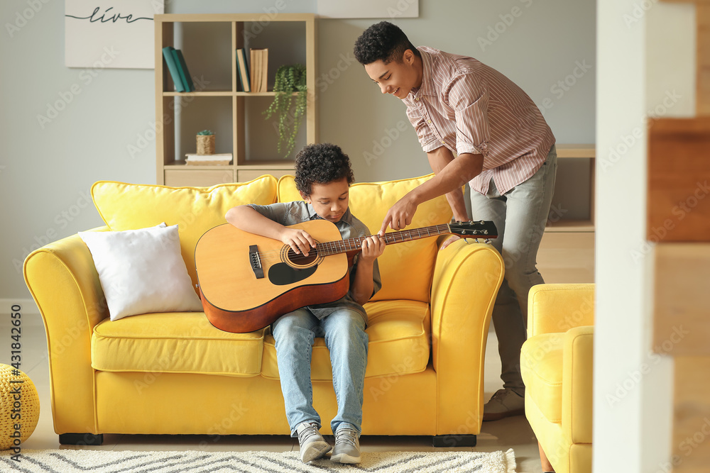 Teenage boy teaching his little brother to play guitar at home