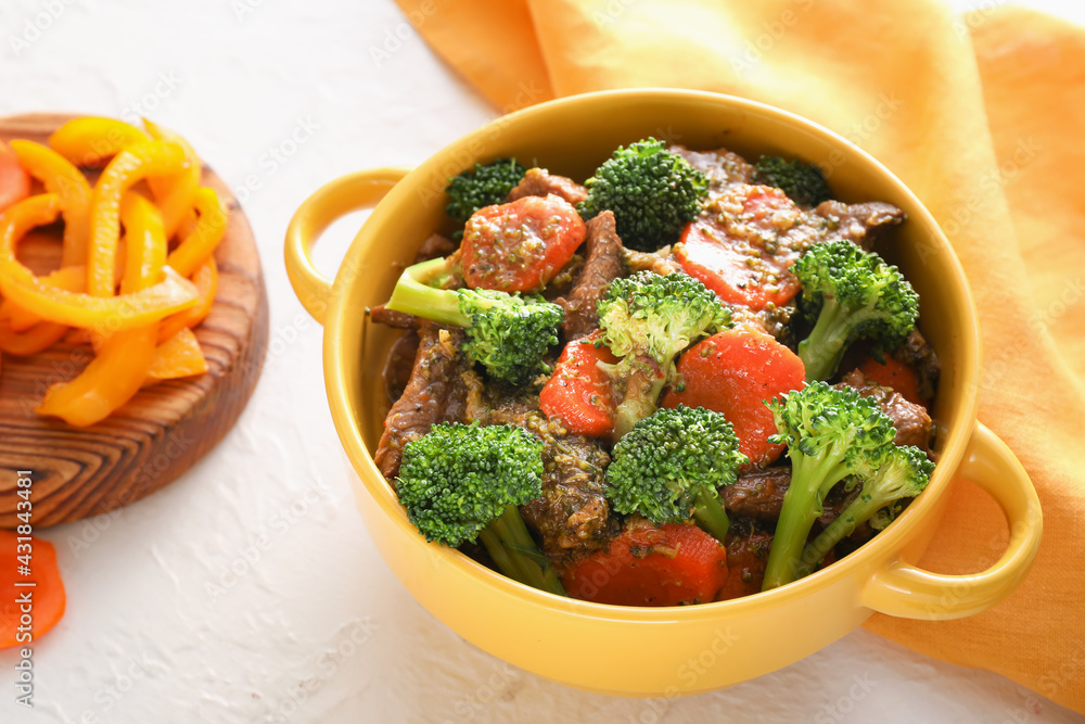 Bowl with tasty beef and vegetables on light background