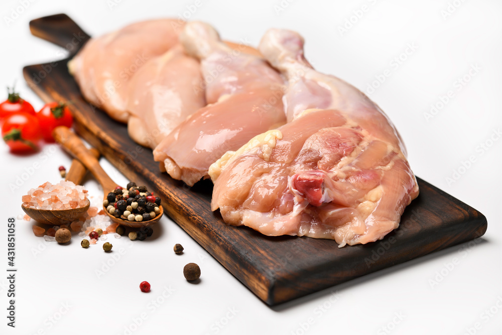 Skinless raw chicken thighs with ingredients for cooking on a wooden cutting board on white backgrou