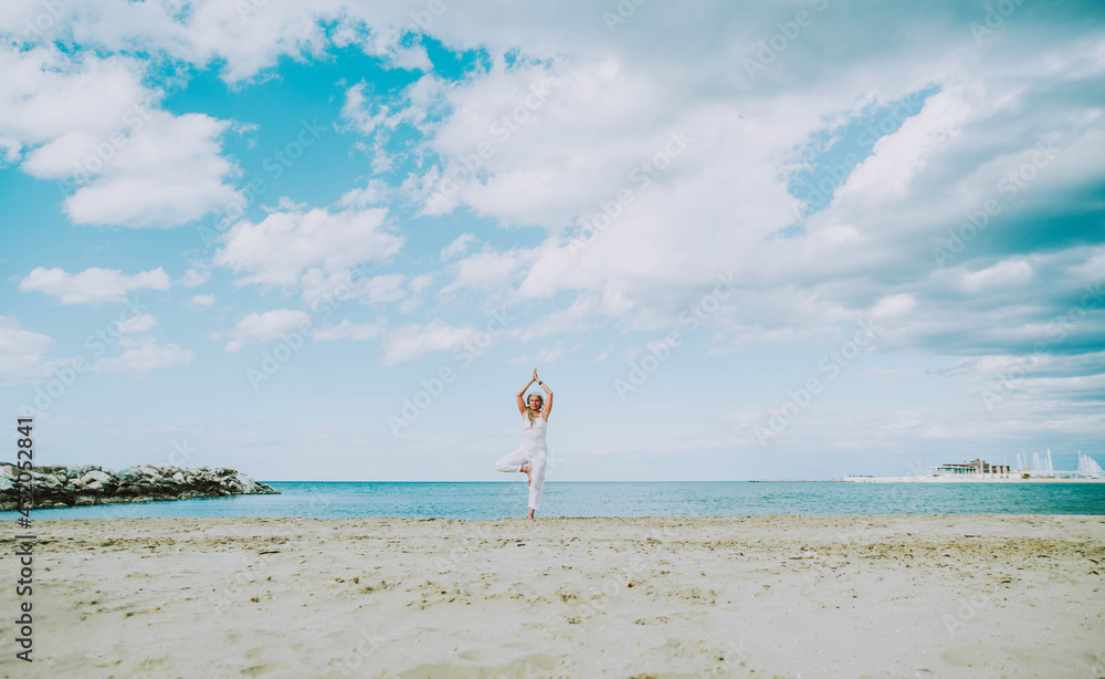 Senior woman doing yoga exercise tree pose at beach - Calm and meditation concept