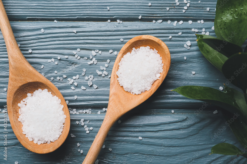 Spoons with salt on wooden background