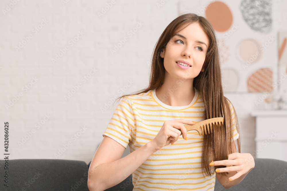 Beautiful young woman combing hair at home