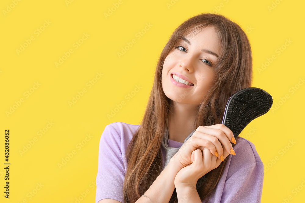 Beautiful young woman with hair brush on color background