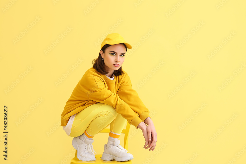 Stylish young woman sitting on chair against yellow background