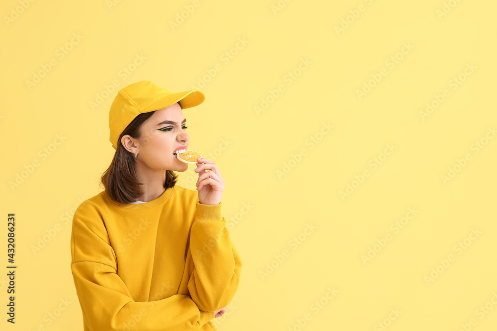 Stylish young woman with orange slice on yellow background