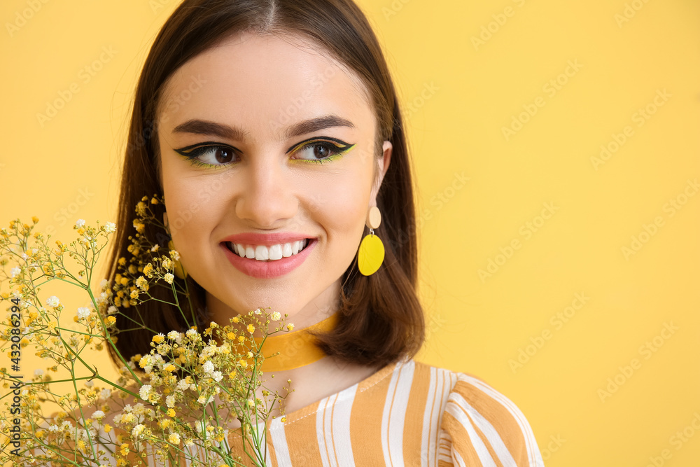 Stylish young woman with flowers on yellow background