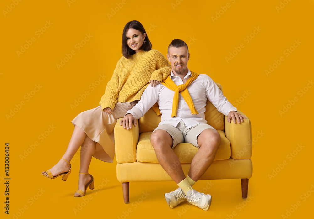 Stylish young couple with armchair on yellow background