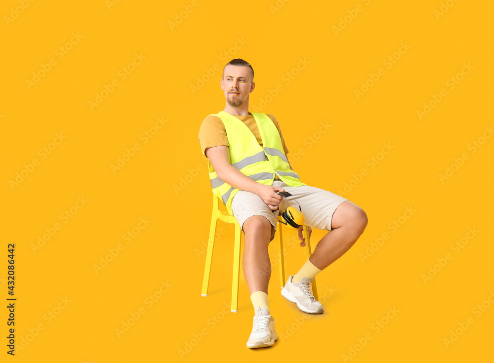 Stylish male worker sitting on chair against yellow background