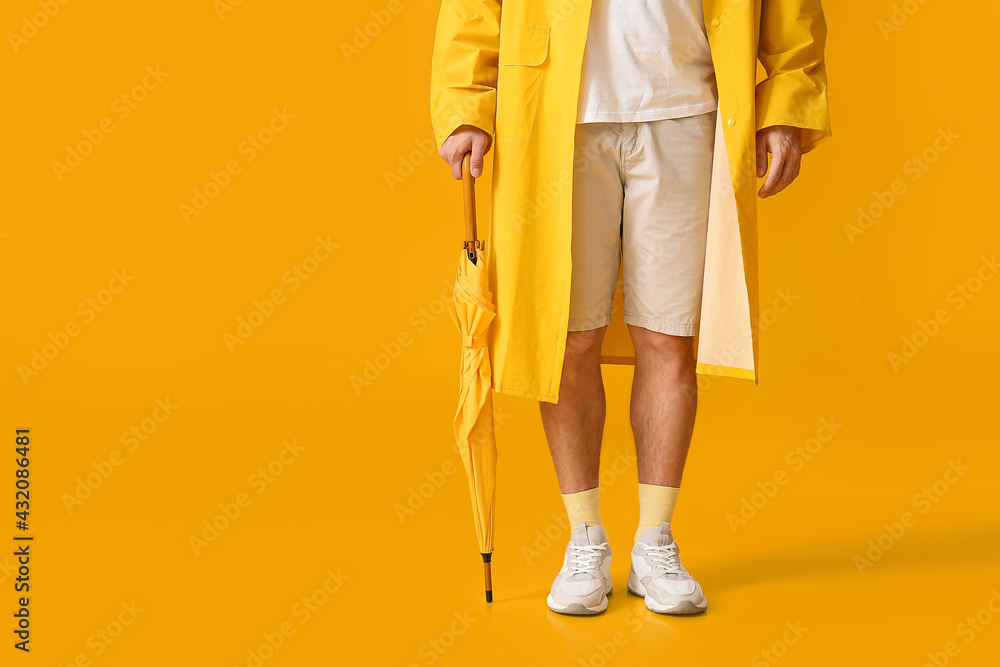 Stylish young man with umbrella on yellow background