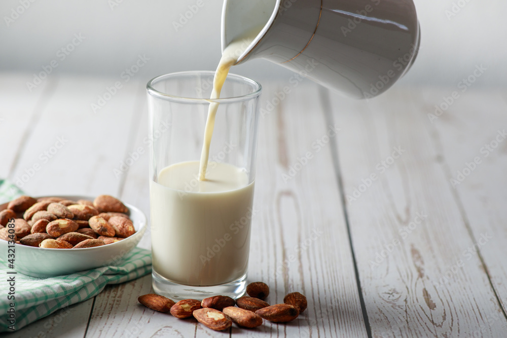 Almond milk in glass with kernel almonds on white wooden background. Healthy eating. Selective focus