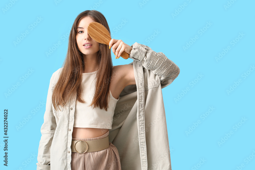 Beautiful young woman with hair brush on color background