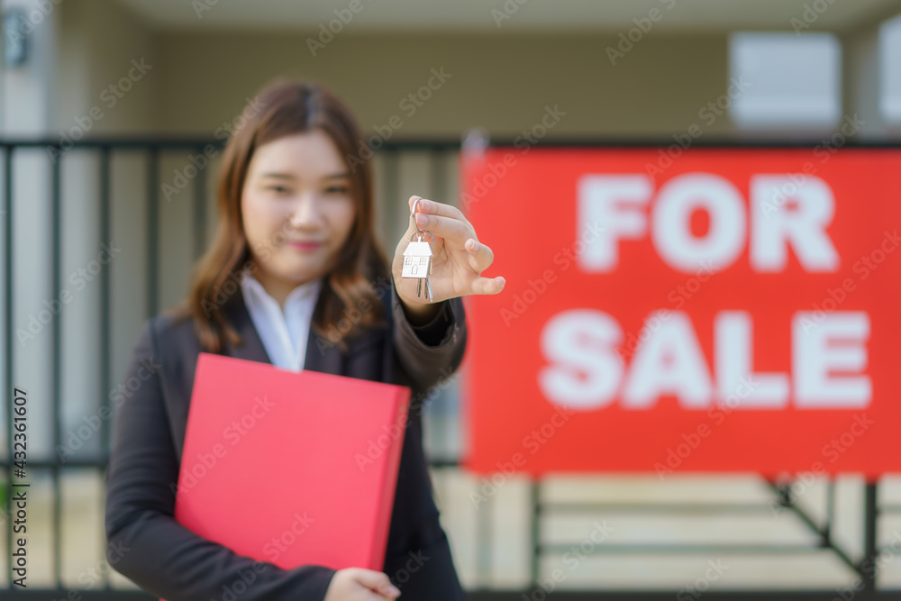 Asian real estate agent or realtor woman smiling and holding red file with showing house key in fron