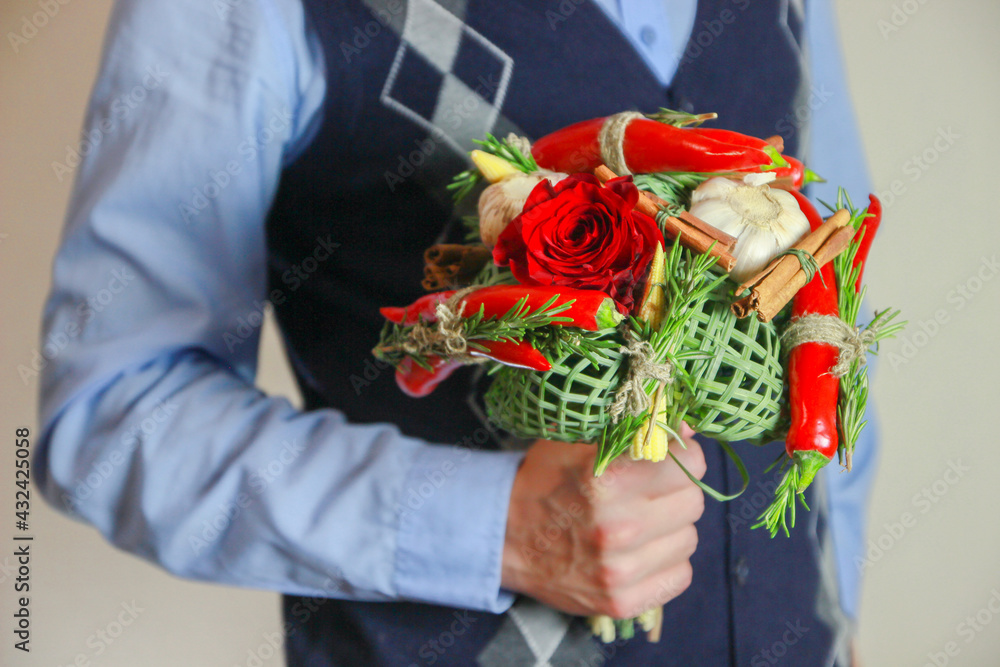 Mens bouquet with red roses, chili peppers, cinnamon sticks, corn and garlic in male hands. Vertica