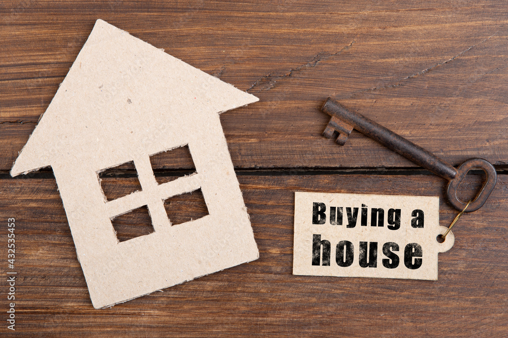 Real estate insurance concept - old key with tag and cardboard house on wooden background