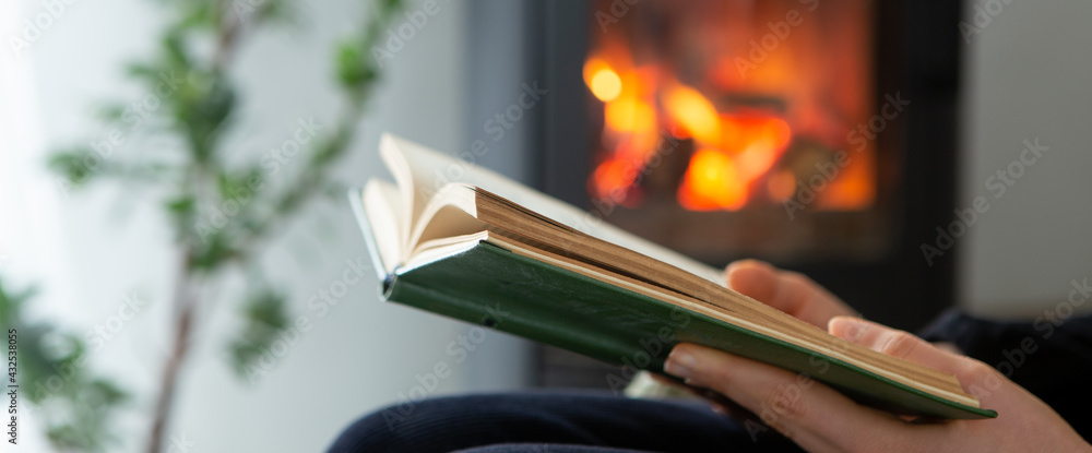 Female reading a book by the fireplace. Cozy winter lifestyle