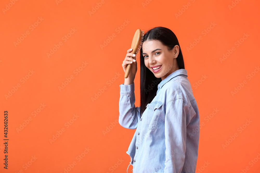 Beautiful young woman with hair brush on color background