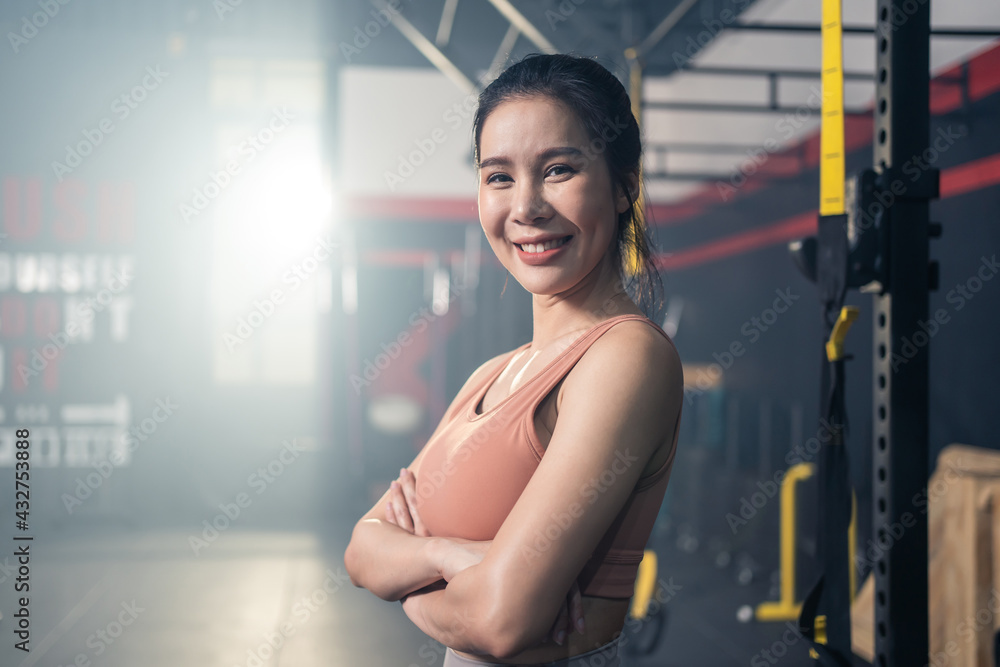 Portrait of Asian female athlete standing and crossing arms in gym.