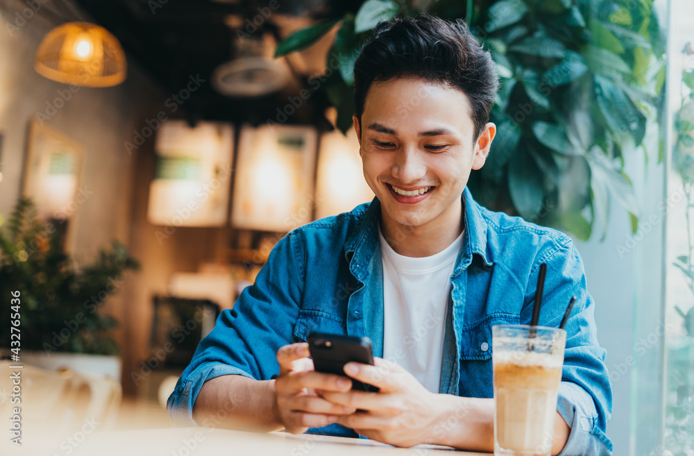 Young Asian man sitting and using smartphone at coffee shop