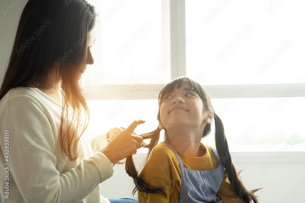 亚洲妈妈坐在家里的床上给女儿编辫子。