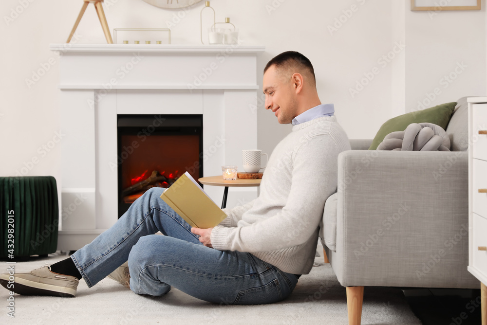 Handsome man reading book near fireplace at home