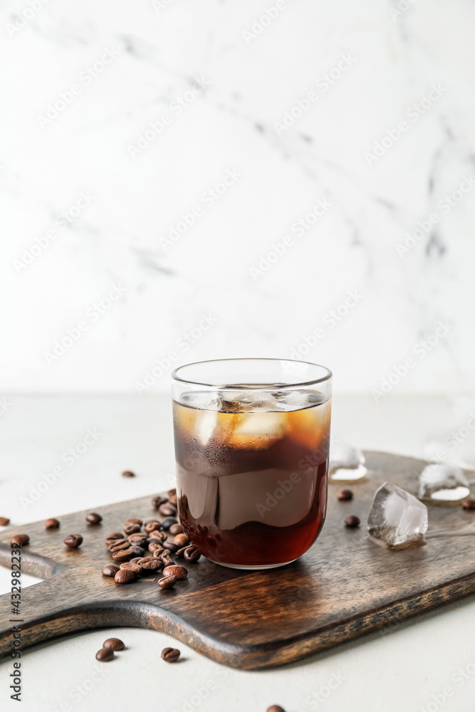 Board with glass of cold brew and coffee beans on light background