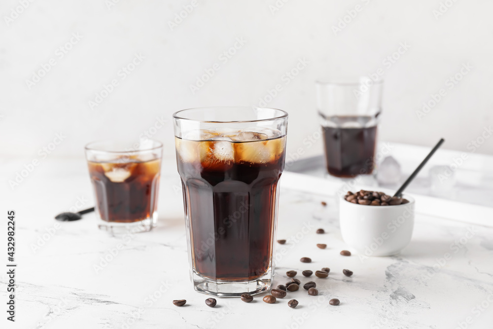 Glasses of tasty cold brew and coffee beans on light background