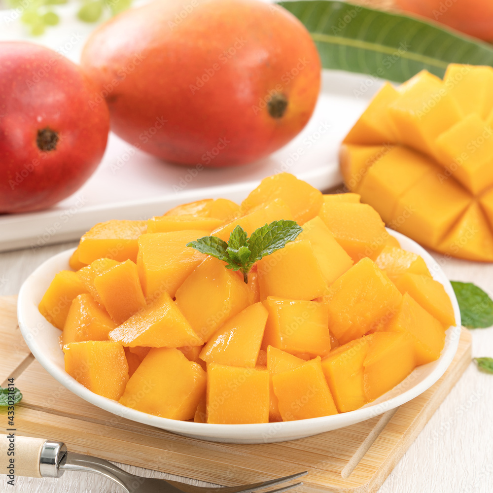 Diced fresh mango fruit on a white plate with leaves.