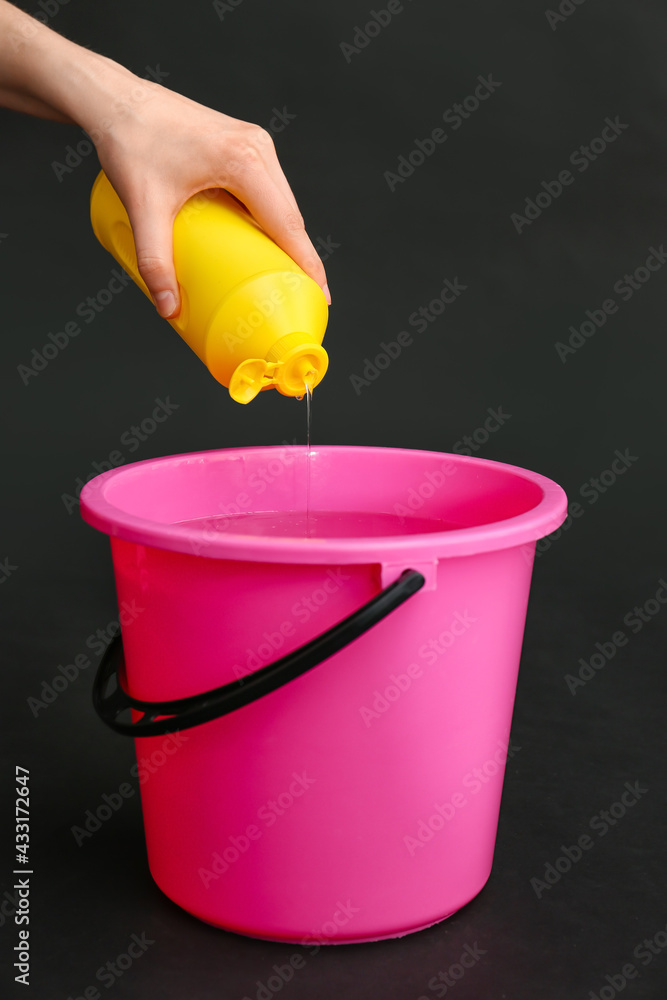 Woman pouring detergent into bucket on dark background