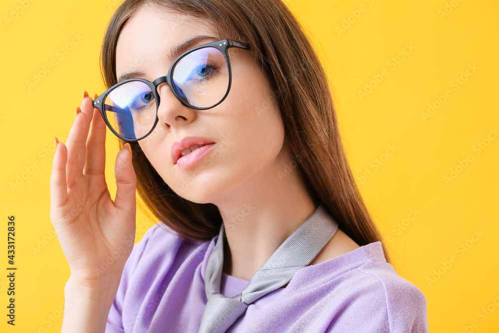 Young woman wearing eyeglasses on color background