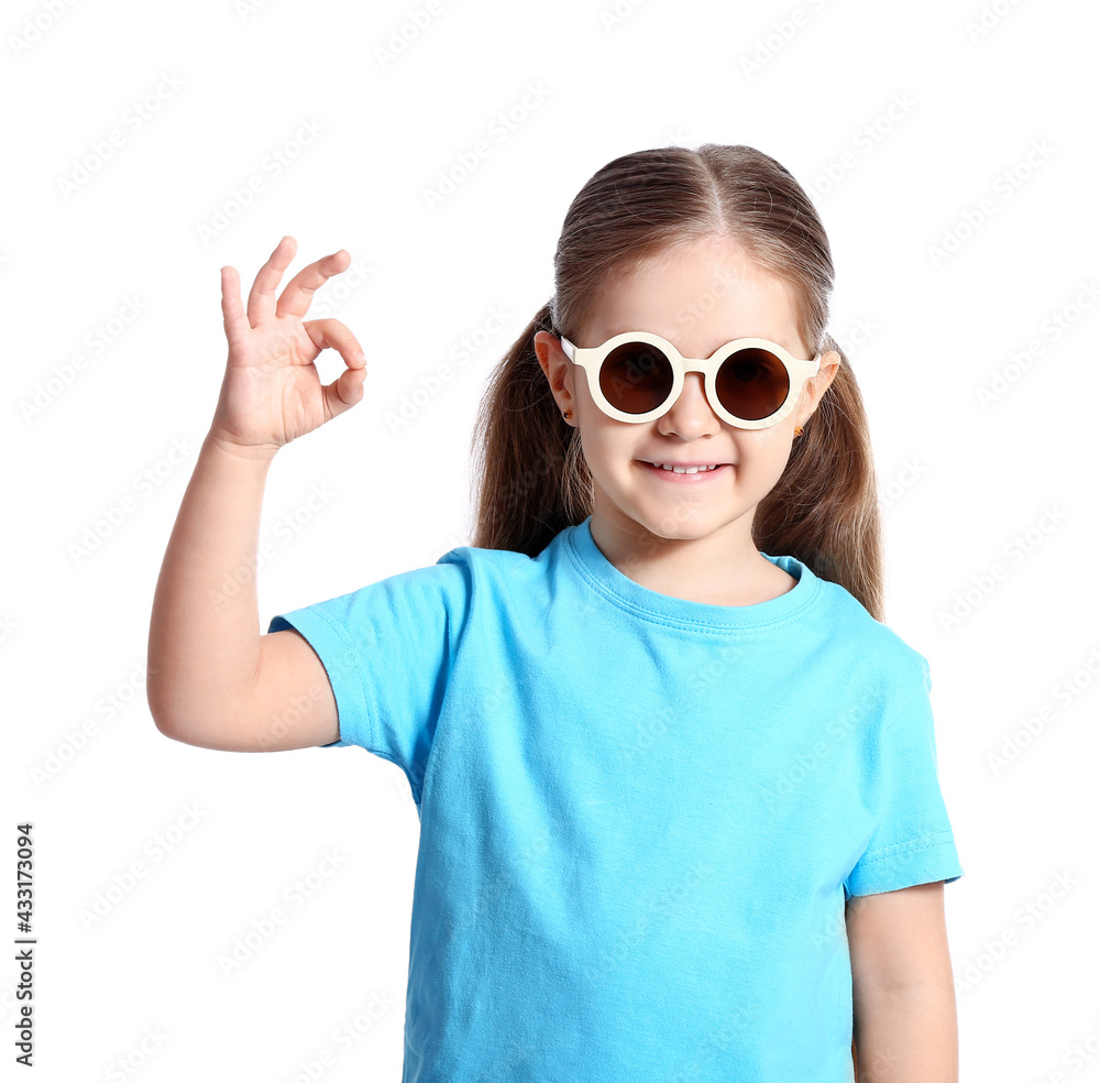 Cute little girl wearing stylish sunglasses and showing OK on white background