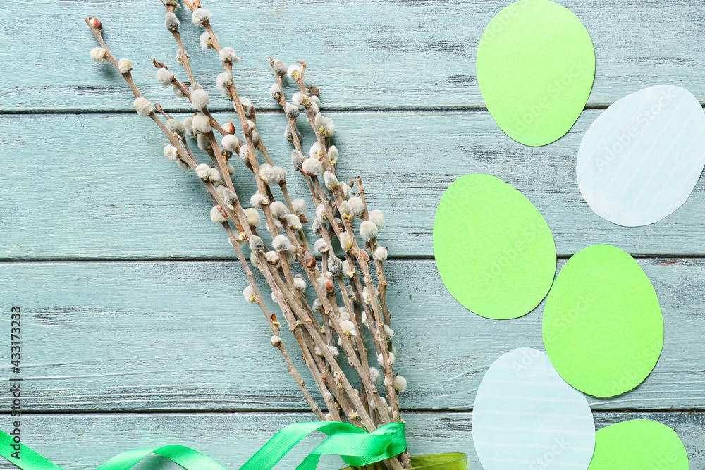 Willow branches and paper eggs on color wooden background