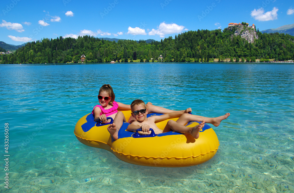 Boy and girl on inflatable float in lake. Little children floating in yellow raft on surface water.