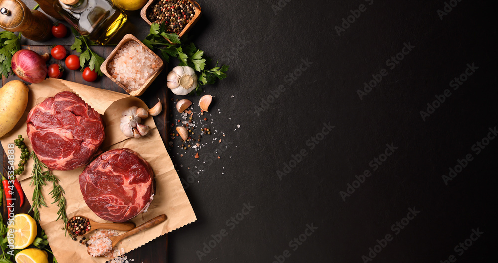 Fresh raw pieces of beef meat with ingredients for cooking on panorama black stone background