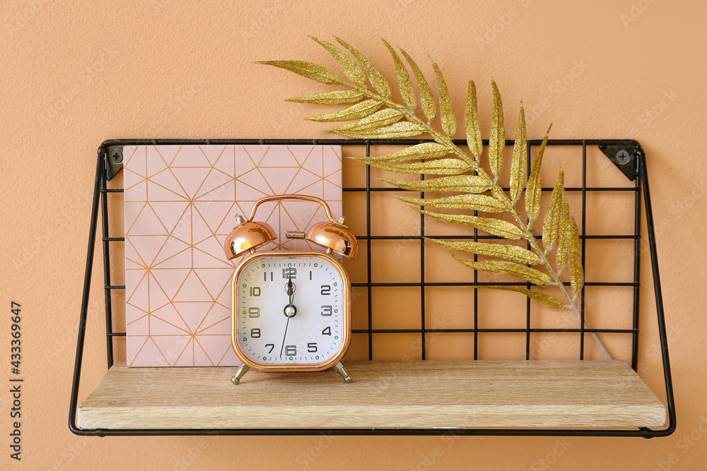 Shelf with alarm clock and decor hanging on color wall